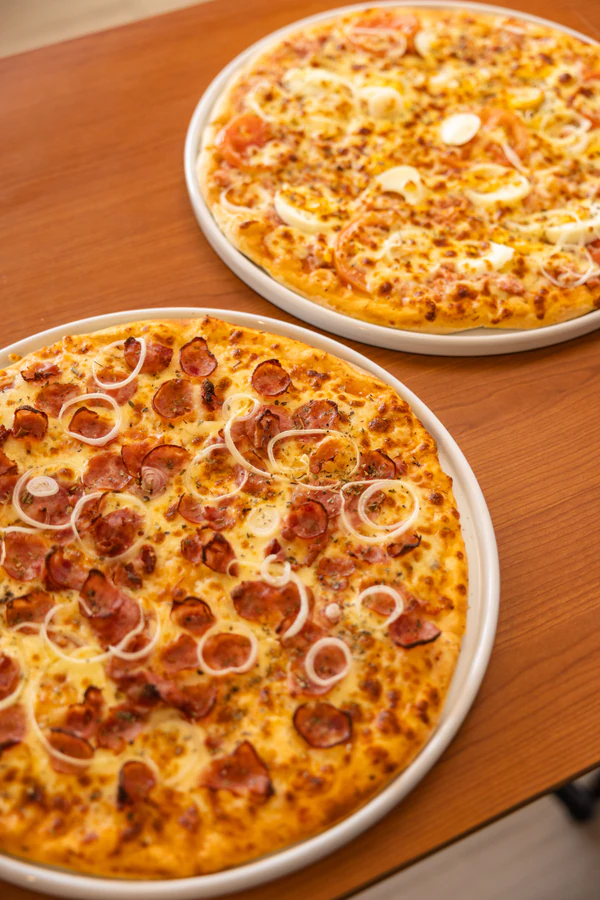 Duas pizzas sobre uma mesa de madeira em fotografia para a Padaria Carone.